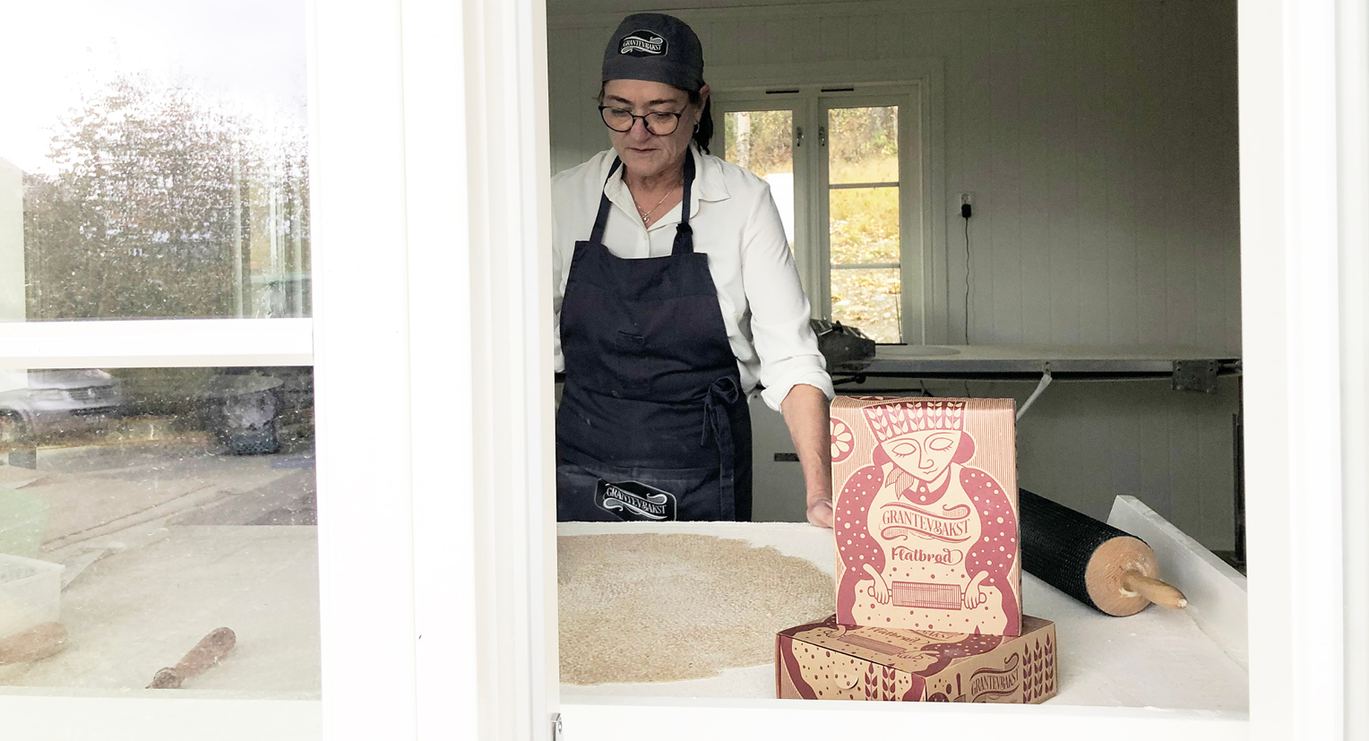 Bilde av bakstekona Jorun hvor hun baker, med embalalsje foran. Emballasjen laget av Haus